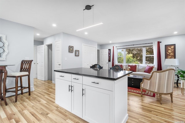 kitchen featuring white cabinetry, a center island, pendant lighting, light hardwood / wood-style floors, and a kitchen bar