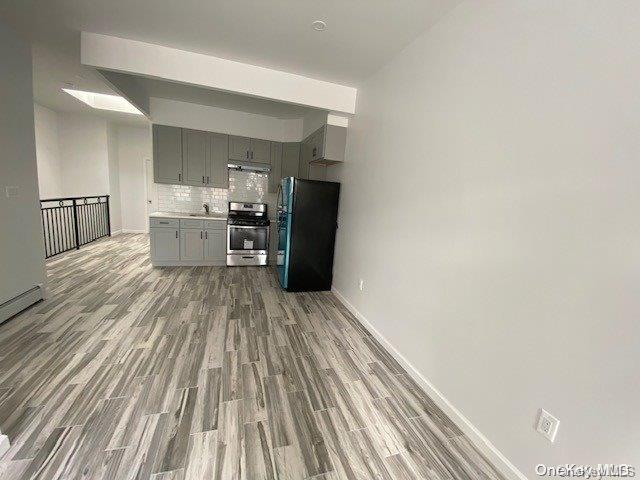 kitchen with backsplash, dark wood-type flooring, black refrigerator, stainless steel stove, and gray cabinets