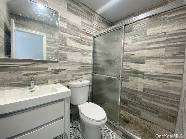 bathroom with vanity, a shower with shower door, tile walls, and toilet