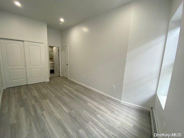 unfurnished bedroom featuring baseboard heating, a closet, and wood-type flooring