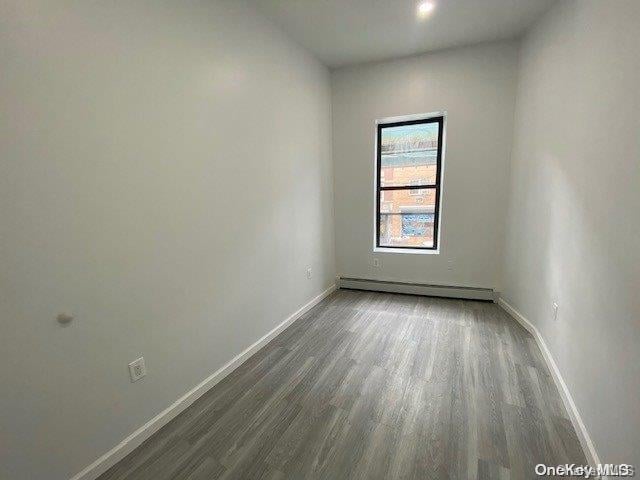 empty room with dark wood-type flooring and a baseboard heating unit