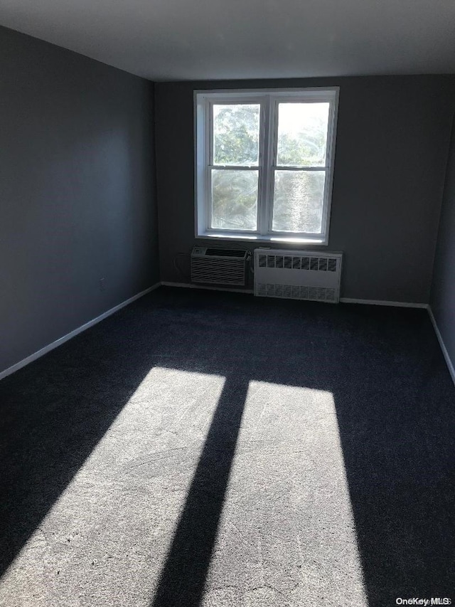 empty room with dark carpet, radiator, and a wall mounted AC