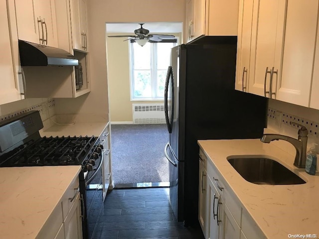 kitchen with light stone countertops, dark hardwood / wood-style flooring, sink, black gas range, and radiator heating unit