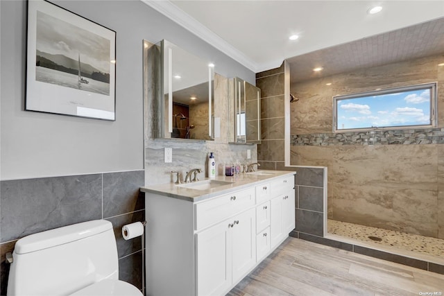 bathroom featuring vanity, toilet, ornamental molding, tile walls, and a tile shower