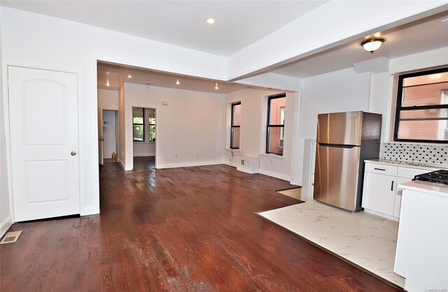 kitchen with white cabinets, wood-type flooring, backsplash, and stainless steel refrigerator