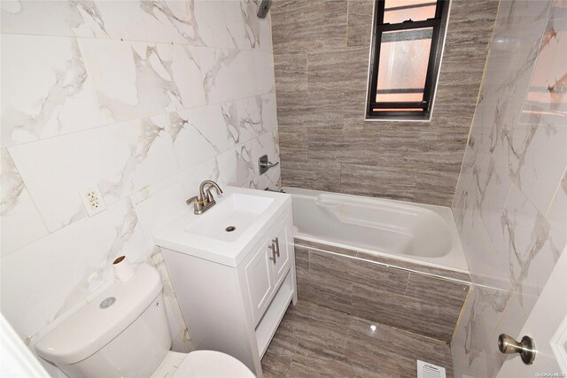 full bathroom featuring vanity, toilet, tile walls, and tiled shower / bath combo