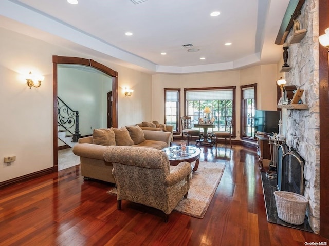 living room featuring dark hardwood / wood-style floors, a stone fireplace, and a tray ceiling