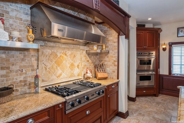 kitchen featuring light stone countertops, stainless steel appliances, tasteful backsplash, and wall chimney range hood