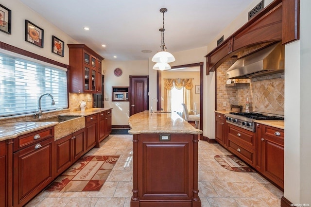 kitchen with a healthy amount of sunlight, an island with sink, exhaust hood, and decorative light fixtures