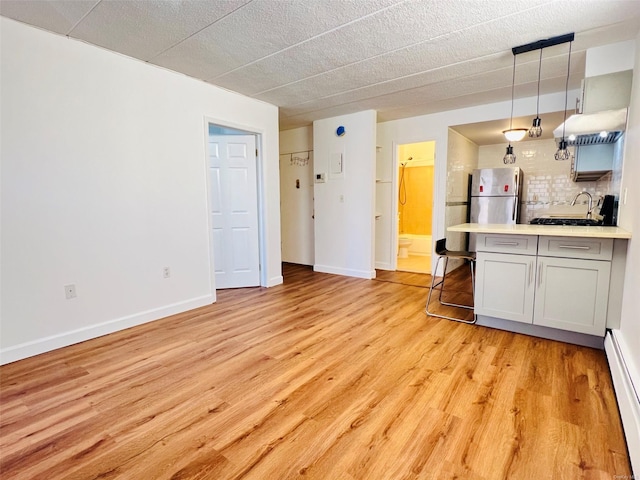 kitchen featuring a baseboard radiator, decorative light fixtures, decorative backsplash, stainless steel refrigerator, and light wood-type flooring