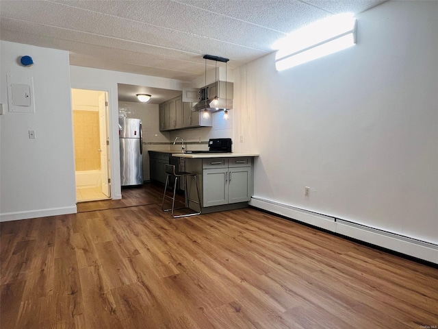 kitchen with a baseboard heating unit, pendant lighting, wood-type flooring, stainless steel refrigerator, and a kitchen breakfast bar