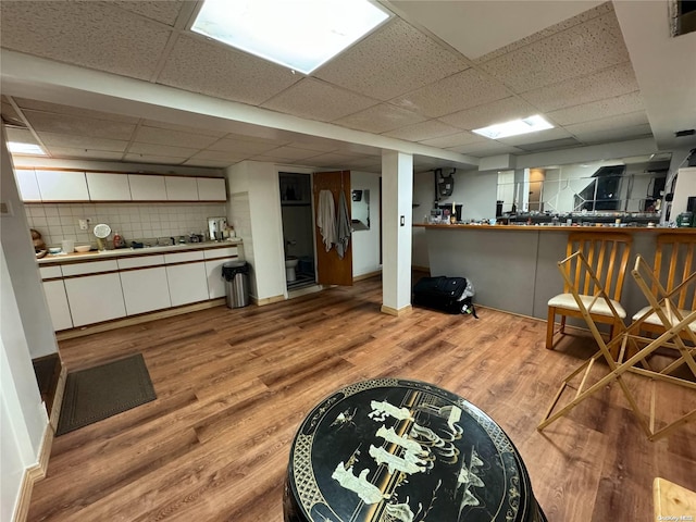 interior space featuring a paneled ceiling, decorative backsplash, light hardwood / wood-style floors, and white cabinetry