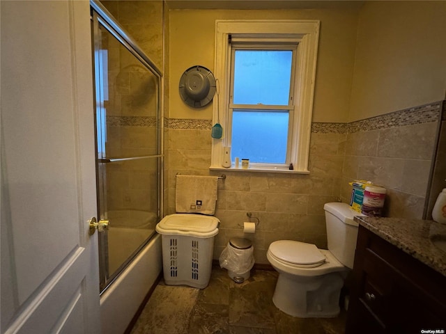 full bathroom with toilet, combined bath / shower with glass door, tile walls, and vanity