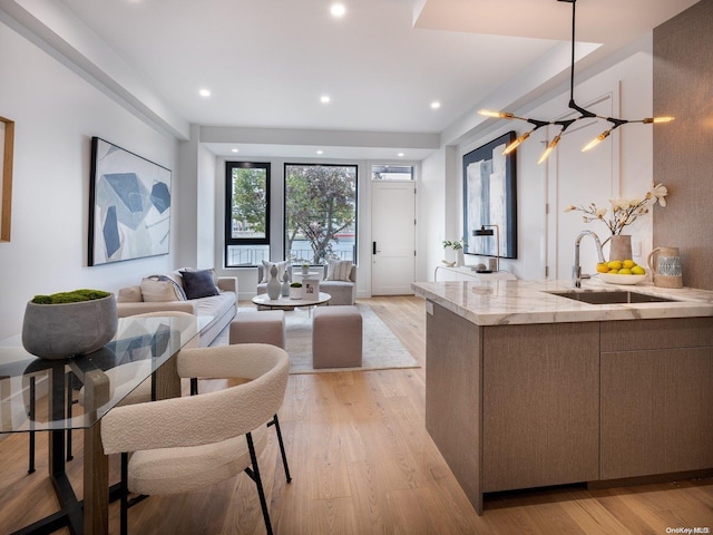 kitchen with light stone counters, sink, decorative light fixtures, and light hardwood / wood-style flooring