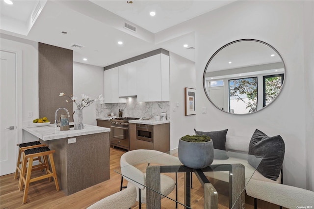 kitchen featuring backsplash, white cabinets, light hardwood / wood-style floors, and appliances with stainless steel finishes