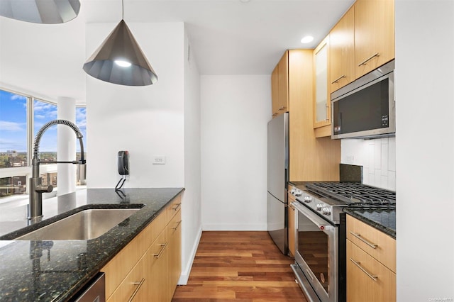 kitchen with sink, hanging light fixtures, stainless steel appliances, dark stone countertops, and light hardwood / wood-style floors