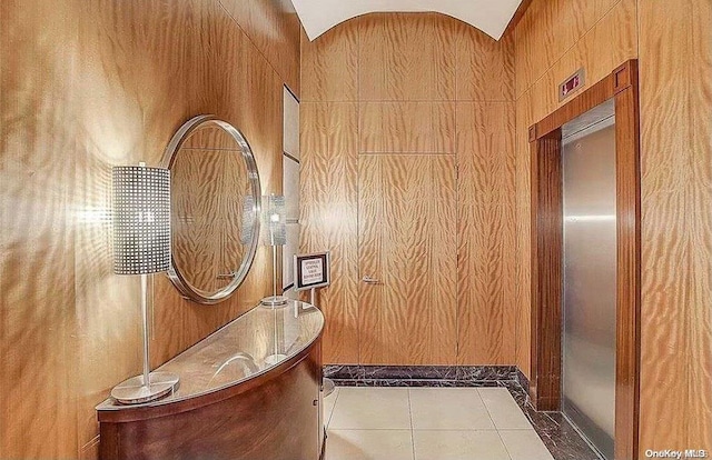 interior space with light tile patterned floors, wooden walls, and vaulted ceiling