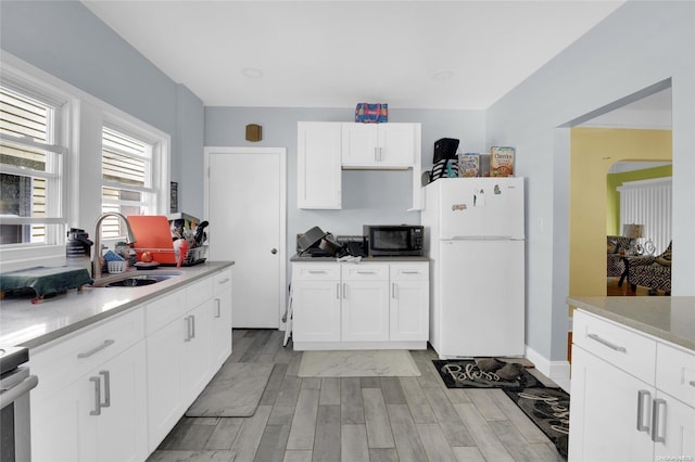 kitchen with white fridge, white cabinetry, sink, and light hardwood / wood-style flooring