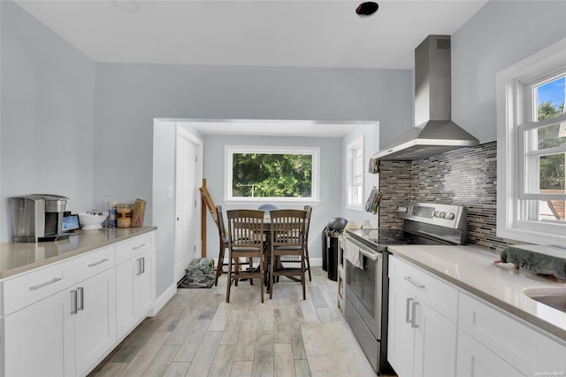 kitchen featuring stainless steel electric stove, white cabinets, wall chimney exhaust hood, light hardwood / wood-style floors, and light stone counters