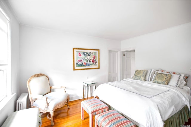 bedroom featuring wood-type flooring, crown molding, radiator, and multiple windows