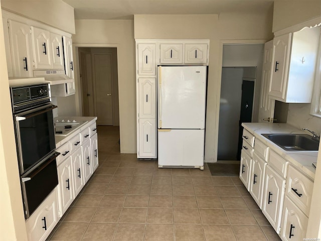 kitchen with light tile patterned flooring, white cabinetry, white fridge, and oven