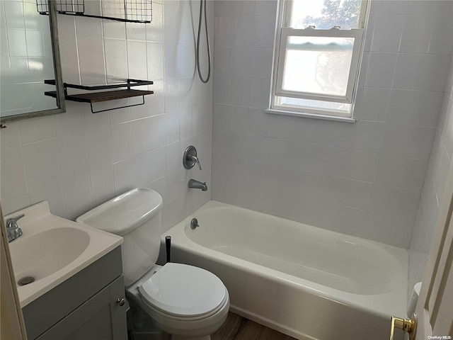 full bathroom featuring tiled shower / bath, hardwood / wood-style floors, tile walls, vanity, and toilet