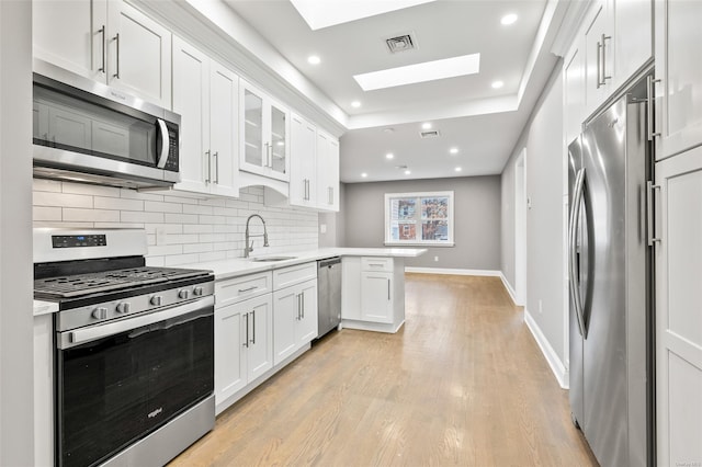 kitchen with kitchen peninsula, appliances with stainless steel finishes, a skylight, sink, and white cabinets