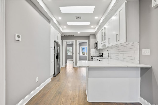 kitchen featuring kitchen peninsula, a skylight, stainless steel appliances, sink, and white cabinetry