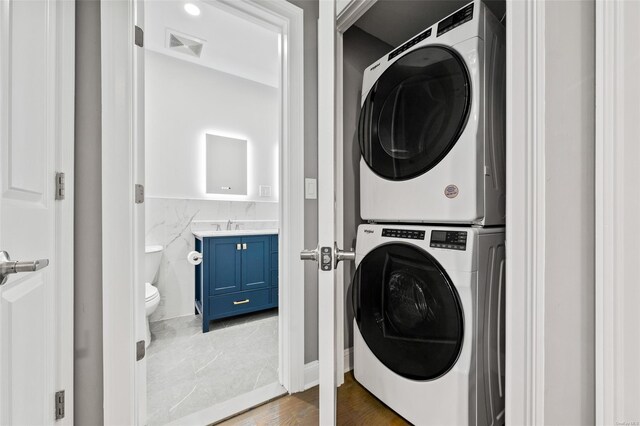 laundry area featuring dark hardwood / wood-style flooring, tile walls, and stacked washer and clothes dryer