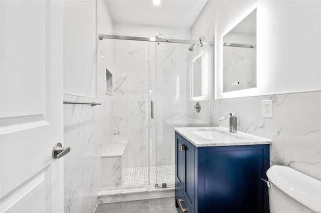 bathroom with vanity, toilet, a shower with shower door, and tile walls