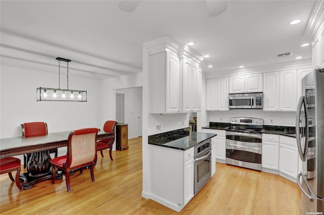 kitchen with dark stone counters, white cabinets, hanging light fixtures, light wood-type flooring, and appliances with stainless steel finishes