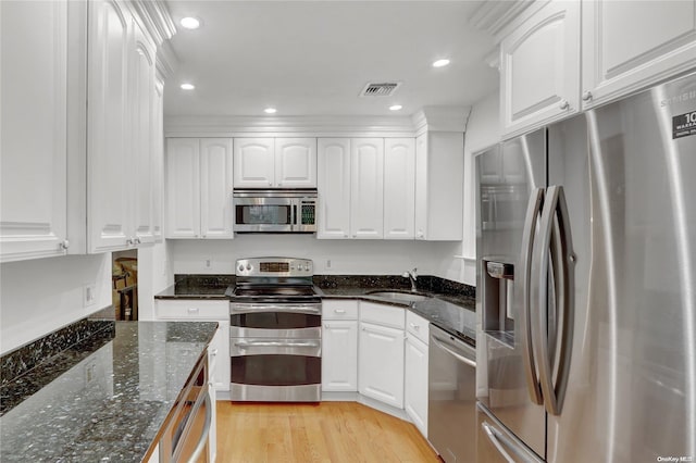 kitchen featuring white cabinetry, sink, dark stone countertops, appliances with stainless steel finishes, and light wood-type flooring