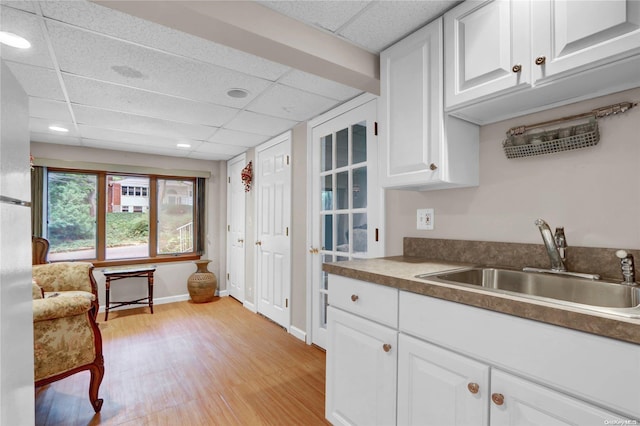 kitchen featuring white cabinets, a paneled ceiling, light hardwood / wood-style floors, and sink