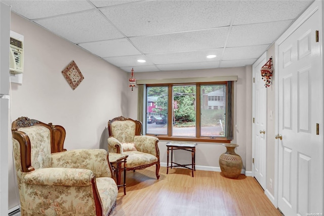 living area featuring a paneled ceiling, wood-type flooring, and a baseboard heating unit