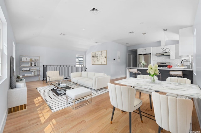 dining space with light hardwood / wood-style floors, lofted ceiling, and sink