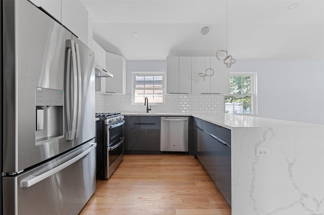 kitchen with pendant lighting, light hardwood / wood-style flooring, appliances with stainless steel finishes, tasteful backsplash, and light stone counters