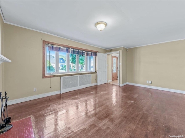 empty room with radiator heating unit, hardwood / wood-style flooring, and ornamental molding