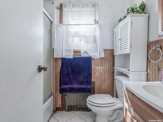 full bathroom with tile patterned flooring, combined bath / shower with glass door, wooden walls, toilet, and vanity