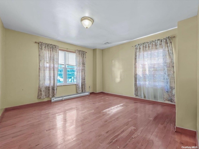 unfurnished room featuring wood-type flooring and a baseboard heating unit