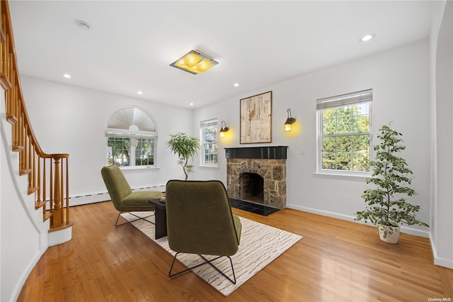 living room with a baseboard radiator, light hardwood / wood-style flooring, and a stone fireplace