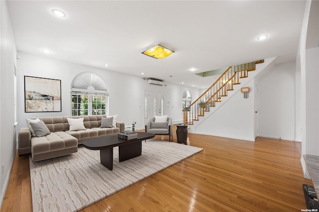 living room with a wall mounted air conditioner and light hardwood / wood-style flooring