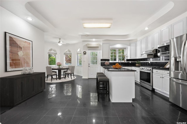 kitchen with white cabinets, a raised ceiling, appliances with stainless steel finishes, a kitchen island, and a kitchen bar