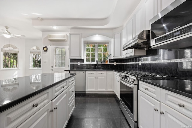 kitchen featuring stainless steel appliances, a wall unit AC, dark stone counters, white cabinets, and exhaust hood