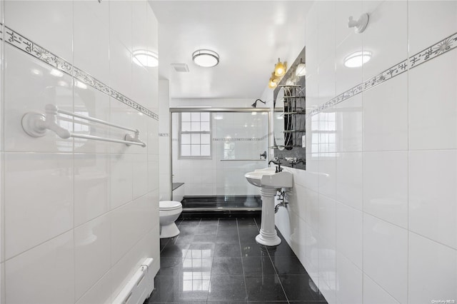 bathroom featuring sink, tile patterned flooring, toilet, a shower with door, and tile walls