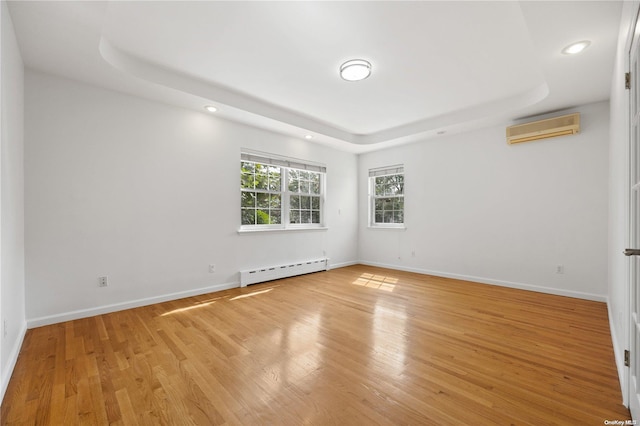 spare room featuring a tray ceiling, light hardwood / wood-style flooring, a wall unit AC, and a baseboard heating unit