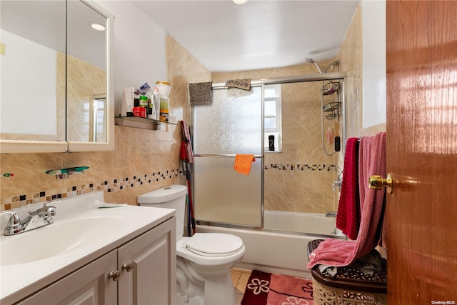 full bathroom with vanity, tile patterned floors, bath / shower combo with glass door, toilet, and tile walls