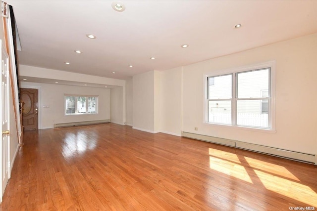 unfurnished living room with light wood-type flooring, a wealth of natural light, and a baseboard radiator