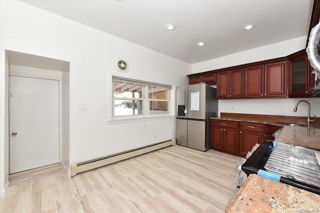 kitchen with stainless steel refrigerator with ice dispenser, light wood-type flooring, a baseboard heating unit, sink, and dark stone countertops