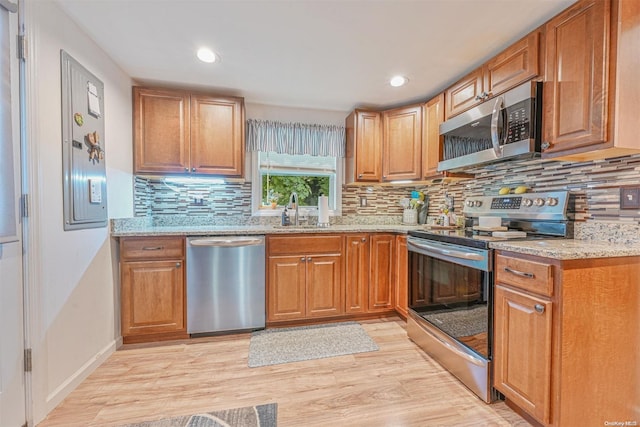 kitchen with appliances with stainless steel finishes, backsplash, light hardwood / wood-style flooring, and light stone counters