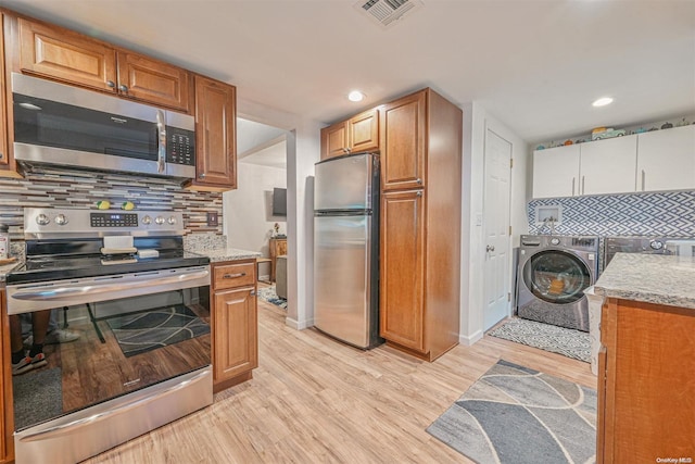 kitchen with tasteful backsplash, light stone counters, stainless steel appliances, independent washer and dryer, and light hardwood / wood-style floors